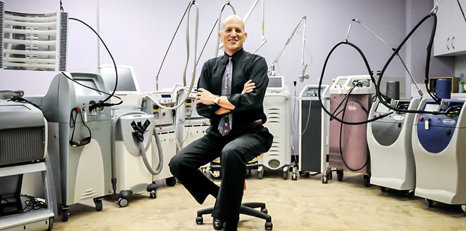 Dr. Asher Milgrom, CEO and Chief Scientist of AMA, with a few of the many lasers used to treat patients at AMA